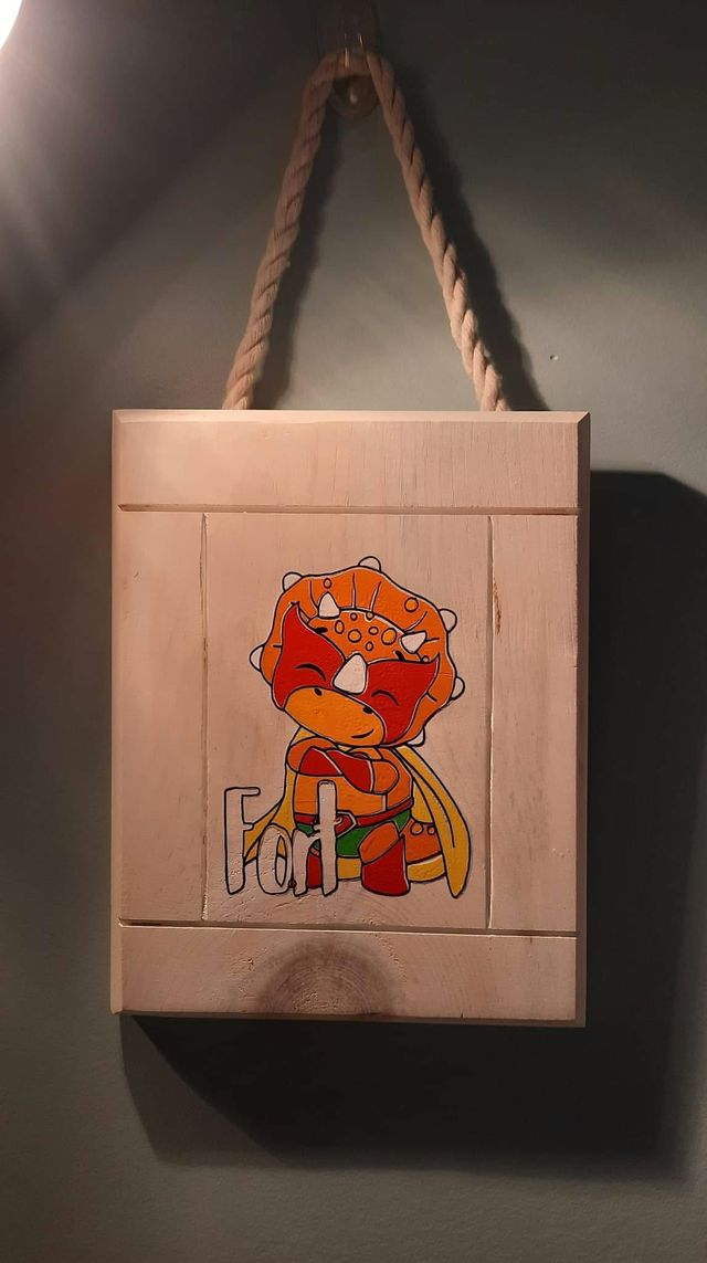 Plaque en bois blanchi suspendue par une corde, ornée d'un tricératops orange en vinyle portant une cape, avec le mot « Fort ».