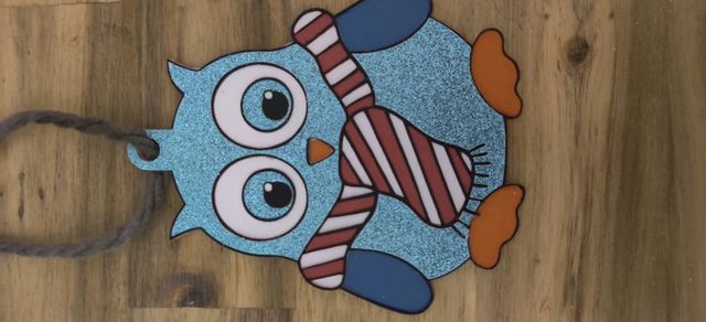 Hibou découpé recouvert de vinyle turquoise pailleté, avec un foulard rayé rouge et blanc, suspendu par une cordelette.