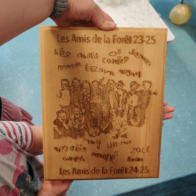 Plaque en bois gravée « Les Amis de la Forêt » reproduisant le dessin d'une photo de groupe d'enfants, entourée de leurs signatures manuscrites.